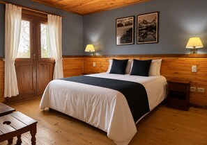 A bedroom with a wooden headboard, a bed with white and dark bedding, two bedside lamps, and two framed pictures on the wall.