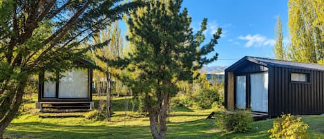 A modern outdoor cabin with a glass door and a small deck, surrounded by lush greenery and trees.