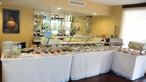 Un montaje tipo buffet con diversos alimentos y bebidas, una vitrina de vidrio y una zona de bar con botellas.
