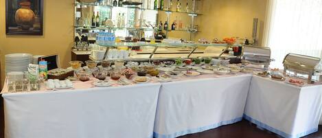 A buffet setup with various food items and beverages, a glass display case, and a bar area with bottles.