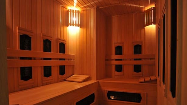 Una sauna con bancos y paredes de madera, incluyendo bancos integrados y un banco con toalla.