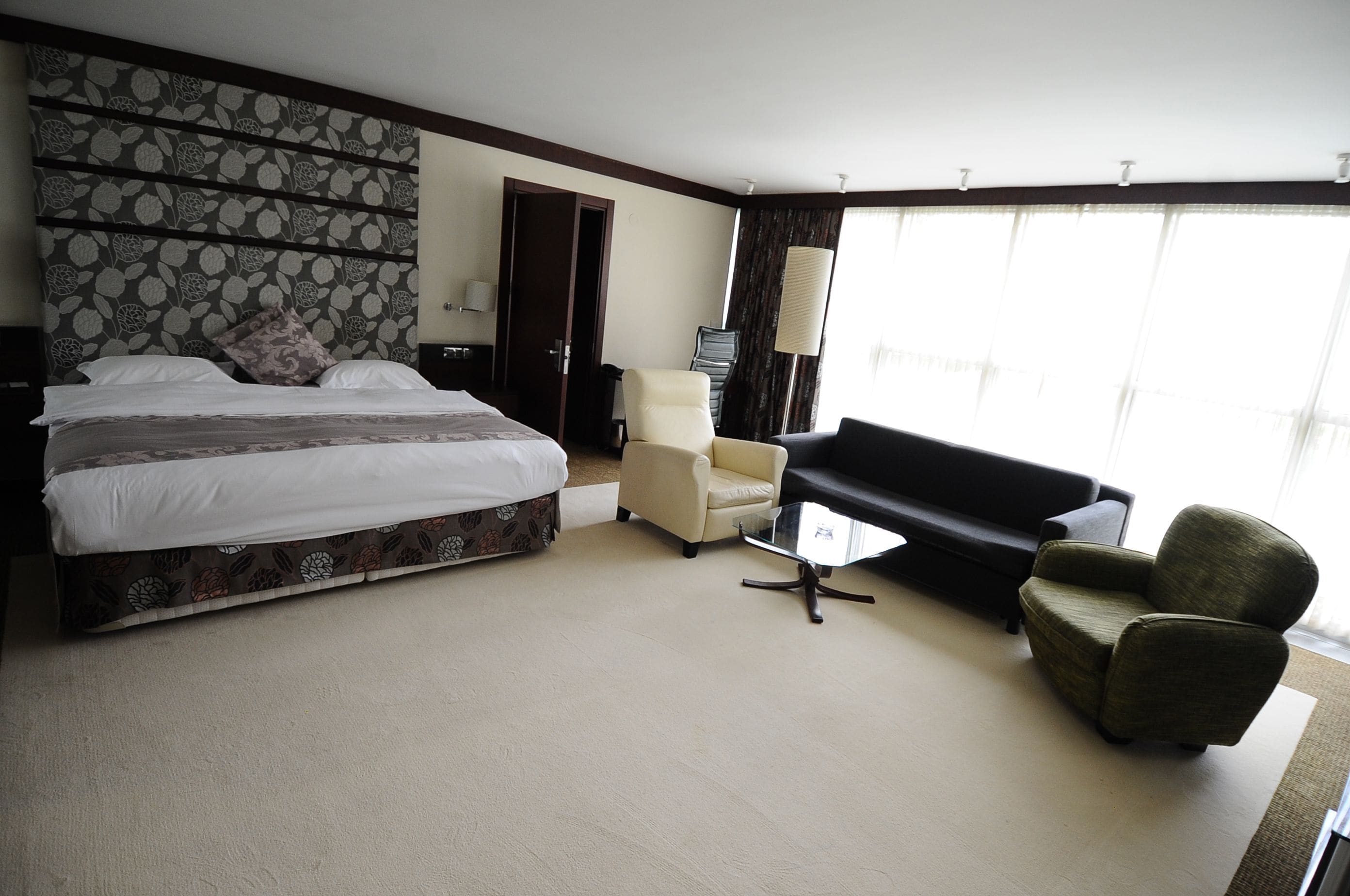 A hotel room with a large bed, a sofa, a chair, and a small table.