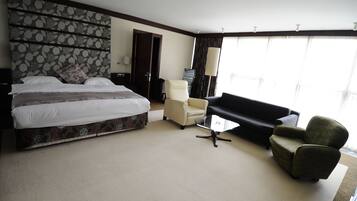 A hotel room with a large bed, a sofa, a chair, and a small table.