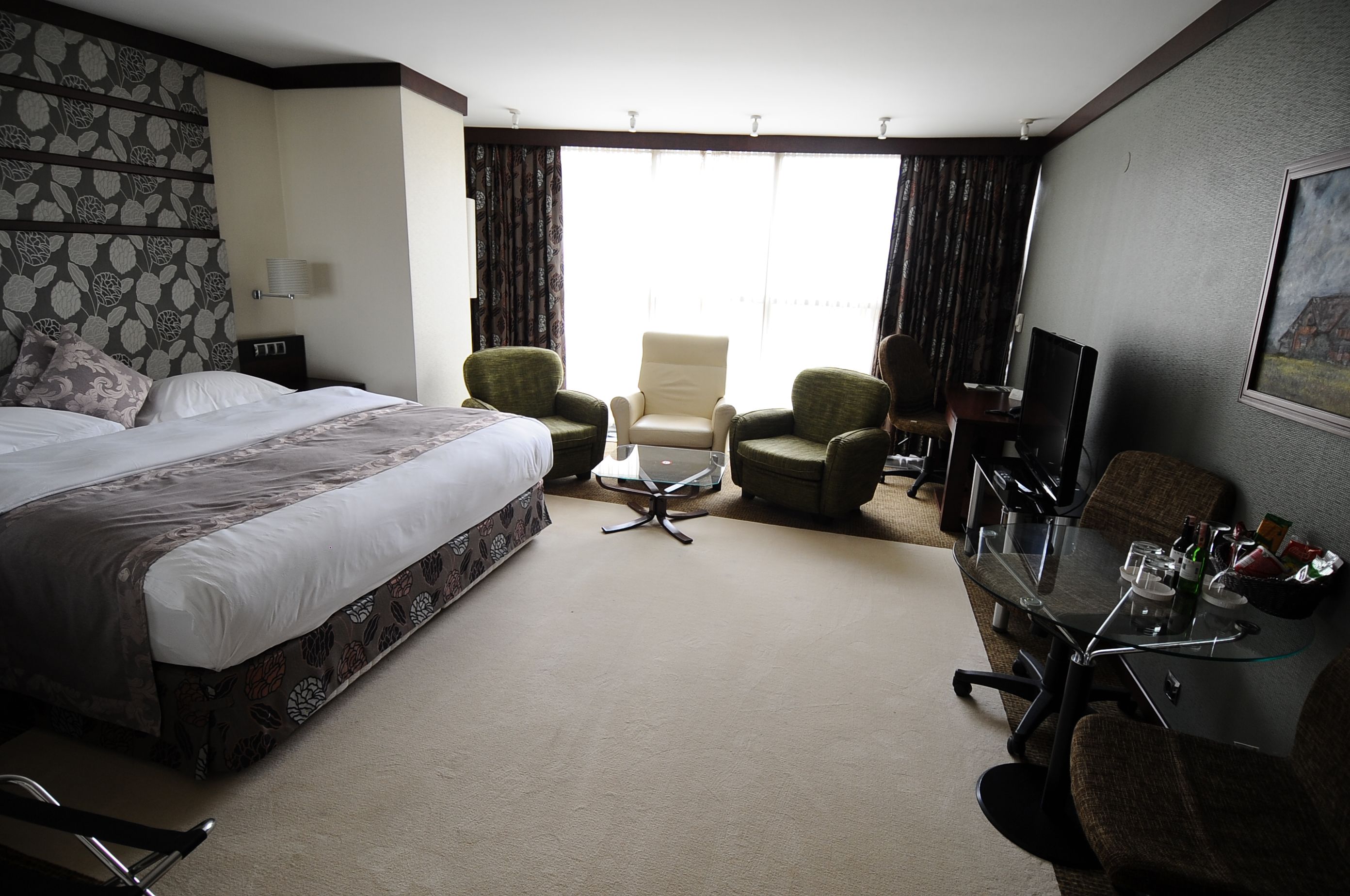 Habitación de hotel con una cama grande, dos sillones, una mesita, un escritorio con computadora y televisión.
