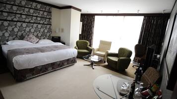 A hotel room with a large bed, two armchairs, a small table, and a glass coffee table.