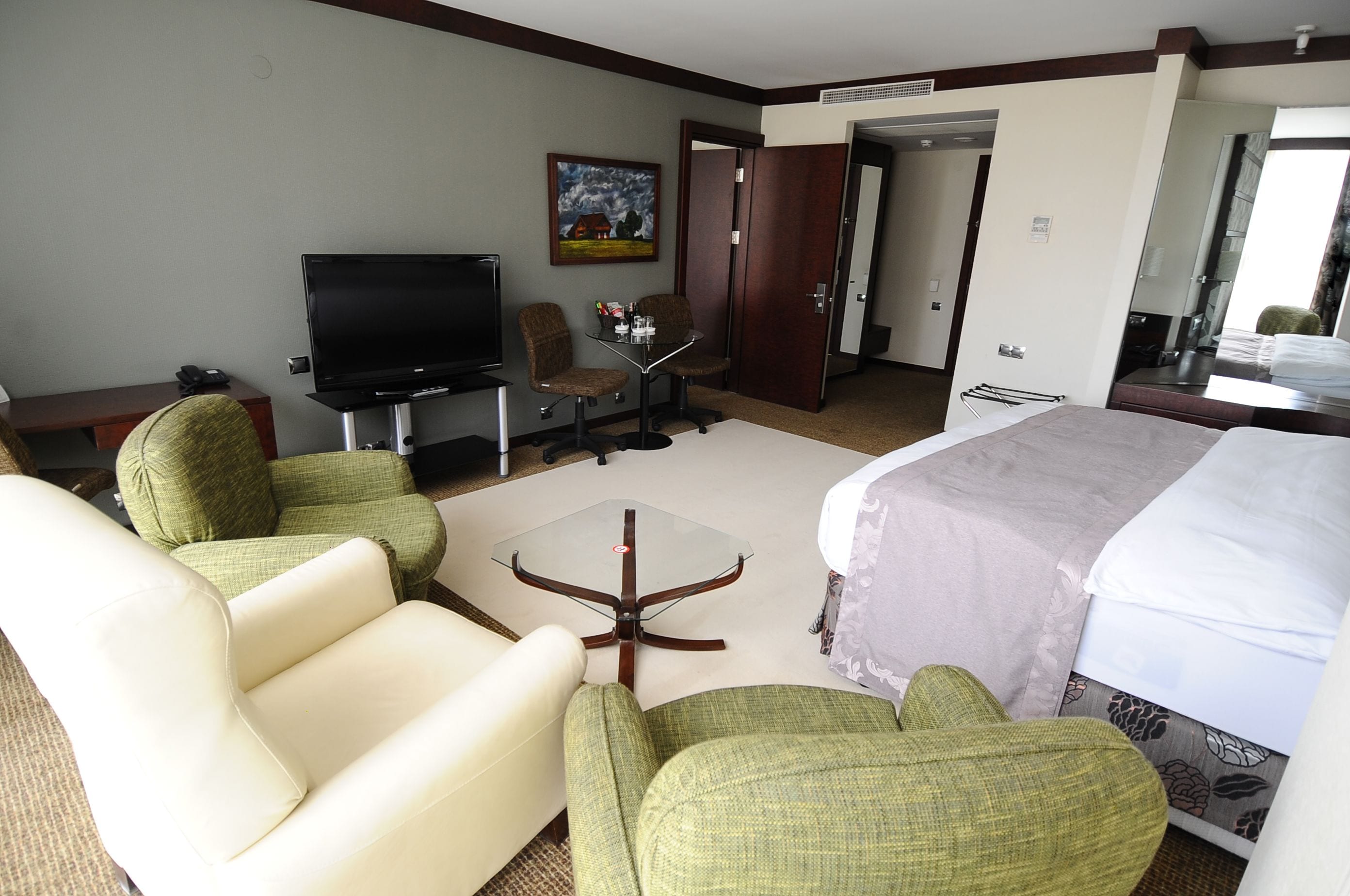 A hotel room with a bed, two armchairs, a small table, a TV, and a door leading to another room.