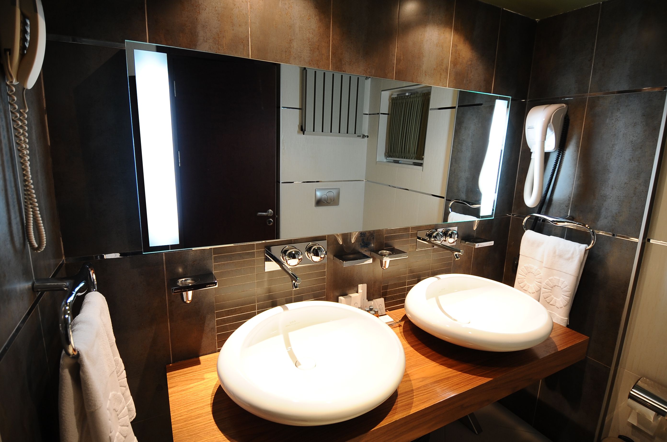 A modern bathroom with two sinks, a large mirror, and a towel rack.