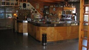 Una zona de bar con barra, estanterías llenas de botellas y una cafetera en el suelo.