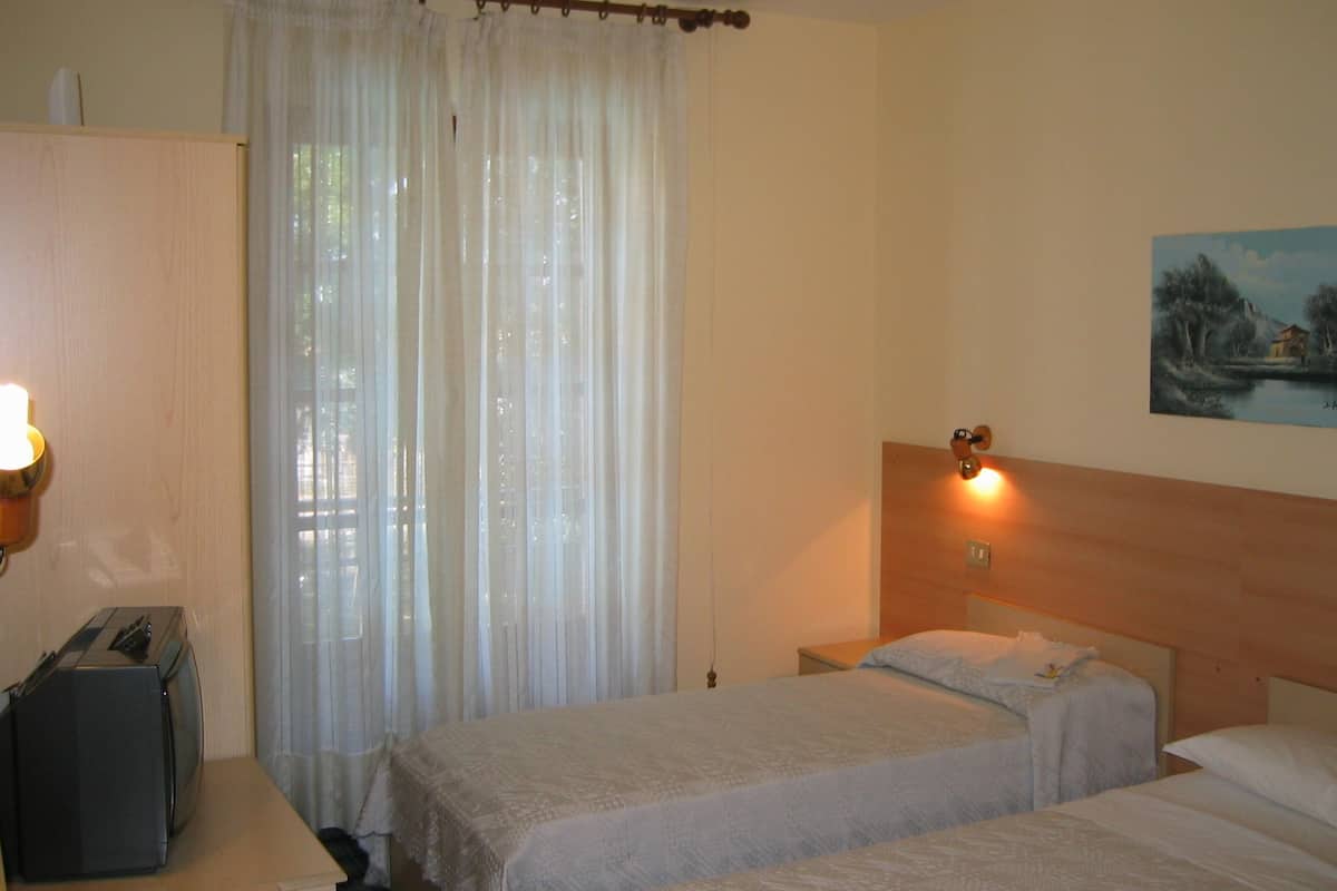 A hotel room with two beds, a wooden headboard, a painting on the wall, and a window with sheer curtains.