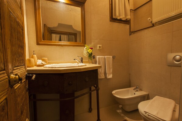 Un baño con tocador de madera, lavamanos, espejo, bidé y perchero para toallas.