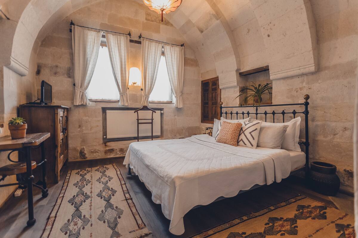 Una camera da letto con un letto grande, una scrivania con un computer, un termosifone e una finestra con tende.