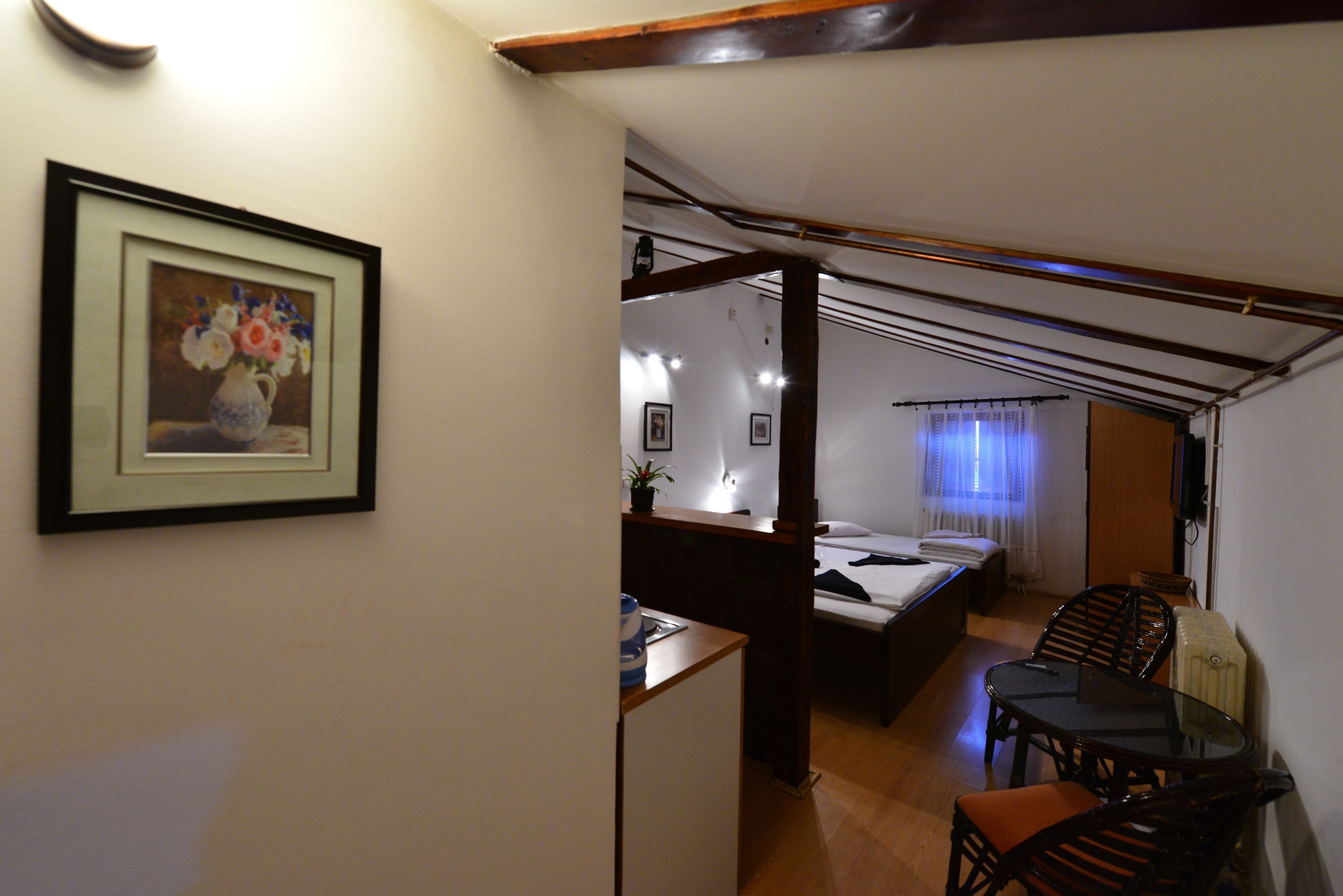 A compact room with a bed, a small table, and a chair. There is a framed picture on the wall.