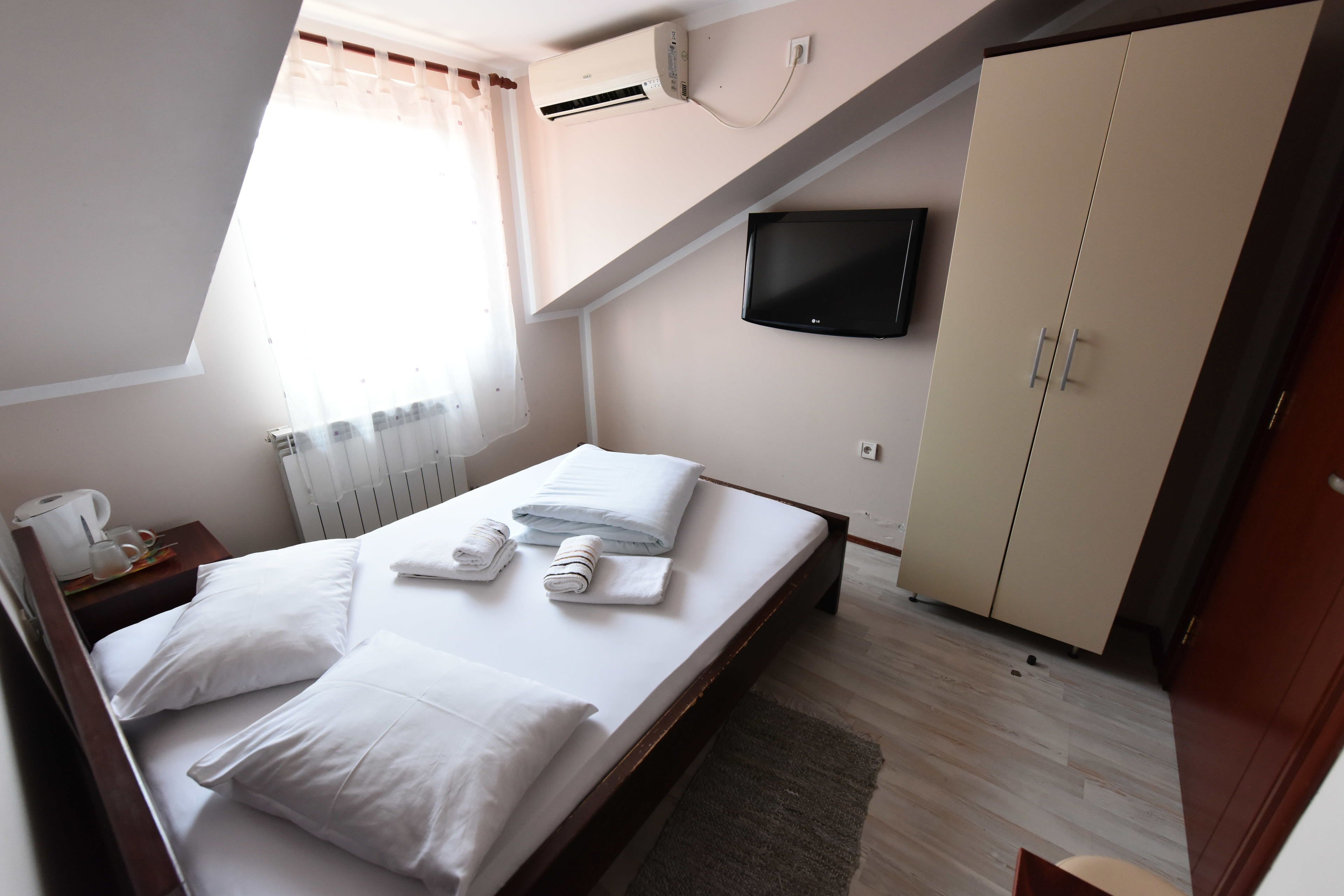Un dormitorio con cama, televisor montado en la pared, armario y ventana con cortinas.