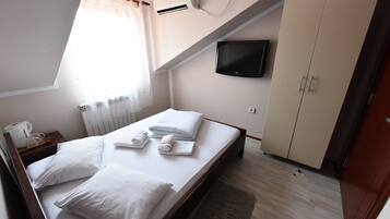 Un dormitorio con cama, televisor montado en la pared, armario y ventana con cortinas.