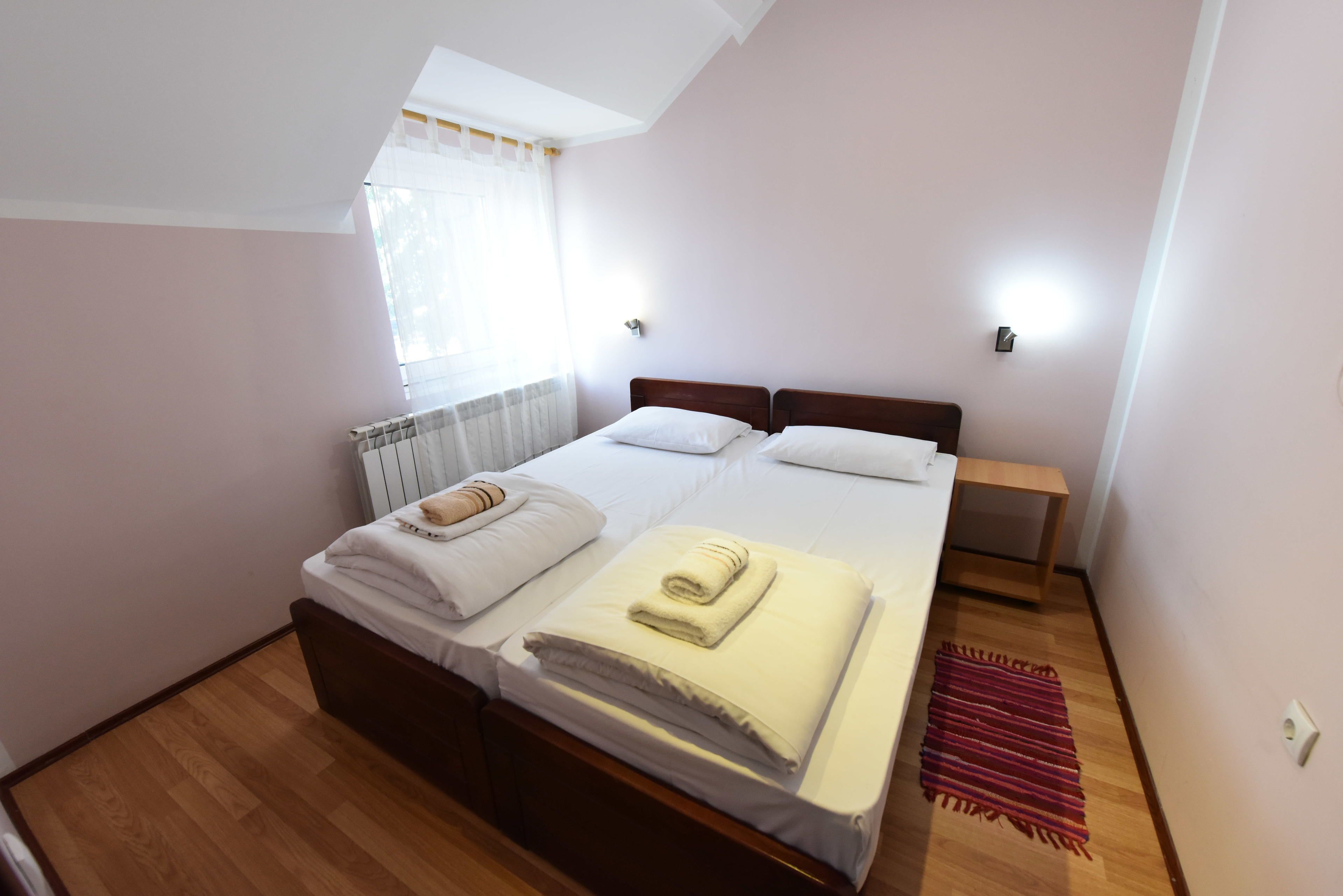 Une chambre à coucher avec un lit en bois, une table de chevet, une petite table, un radiateur et une fenêtre avec des rideaux.