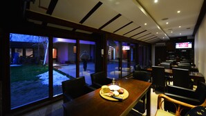 A restaurant with a large window view of the outside, a wooden table with a plate of food, and multiple chairs. - Prenociste Stojic Novi Sad (Novi Sad)