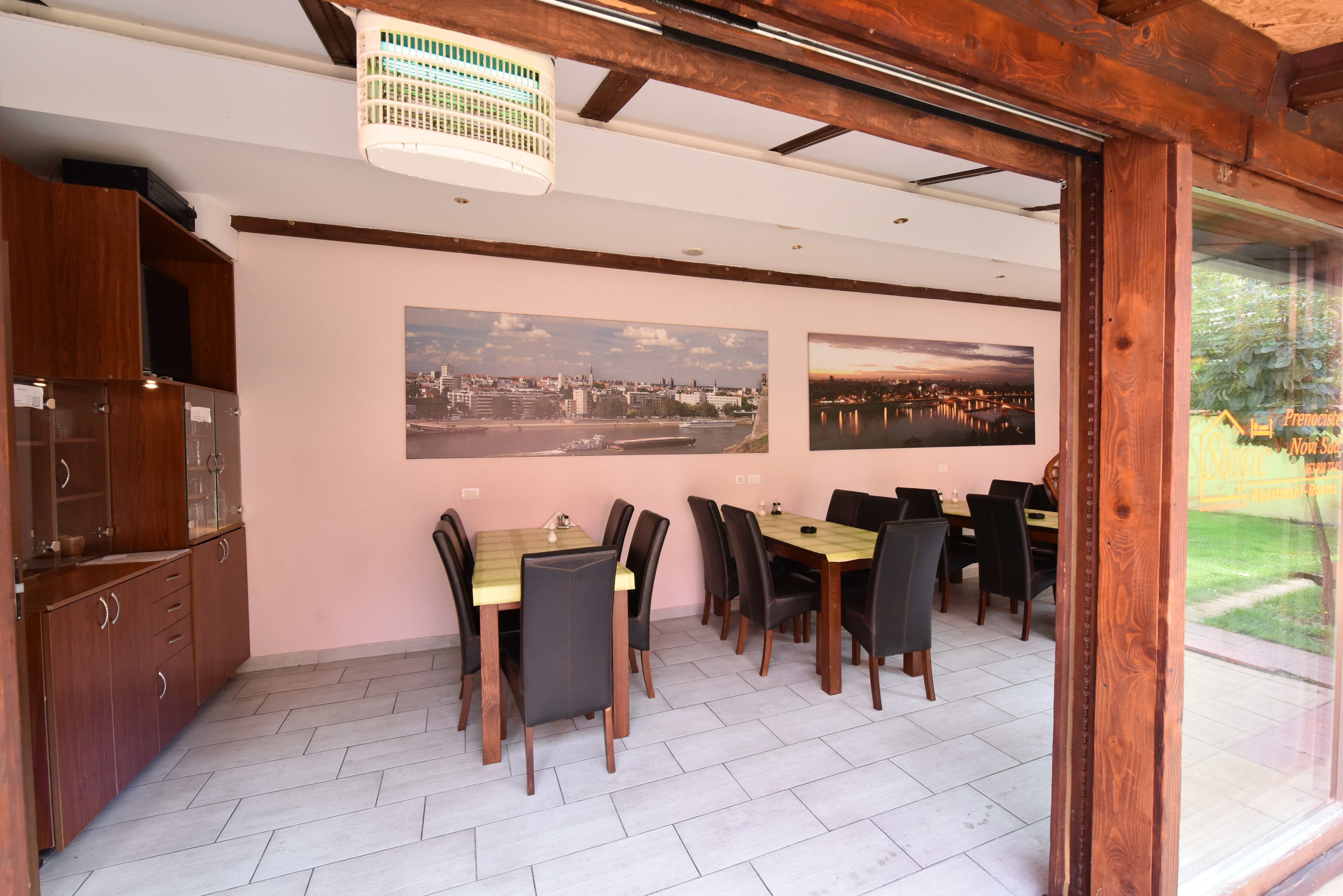 Un comedor con mesas y sillas de madera, un ventilador de techo y dos fotografías de la ciudad en la pared.