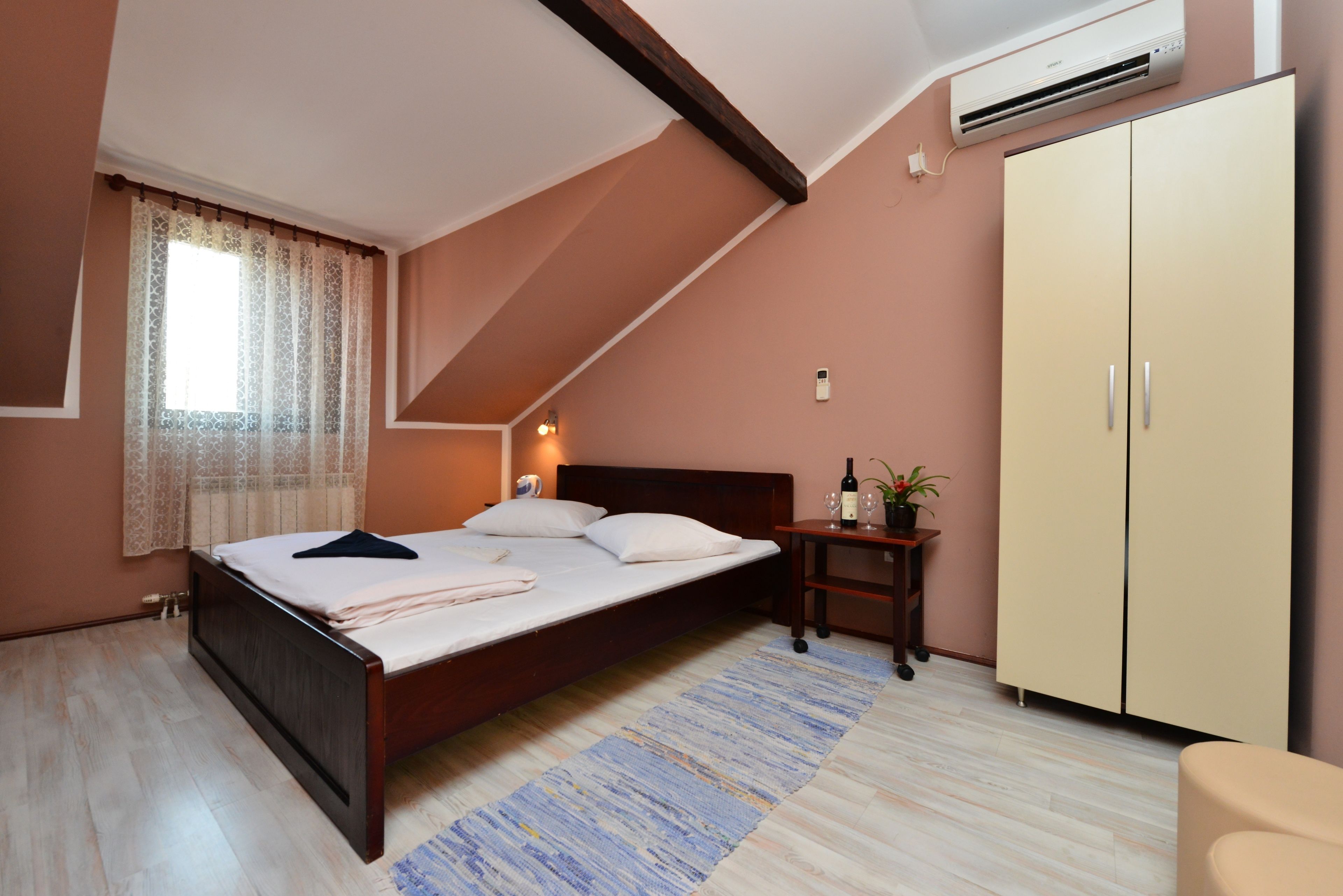 A bedroom with a bed, a nightstand, a wardrobe, and a window with curtains.
