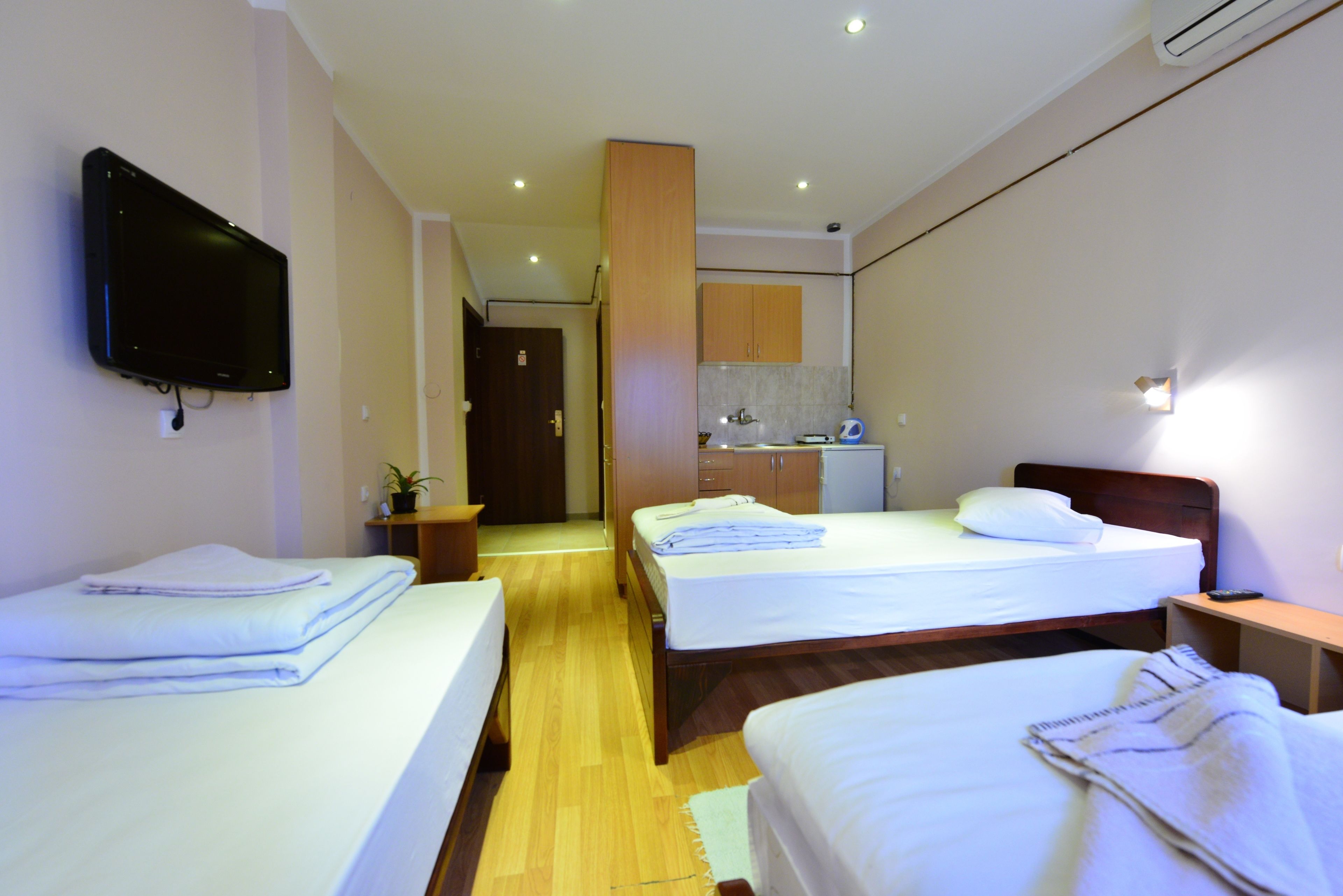 A hotel room with two single beds, a television mounted on the wall, a small kitchenette, and a bathroom visible through an open door.