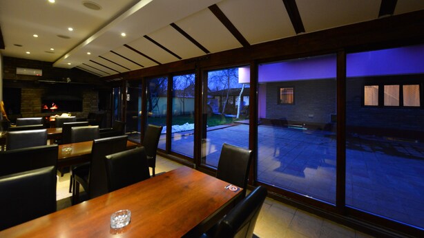 A restaurant with a large wooden table and chairs, a fireplace, and large windows overlooking a snowy outdoor area. - Prenociste Stojic Novi Sad (Novi Sad)