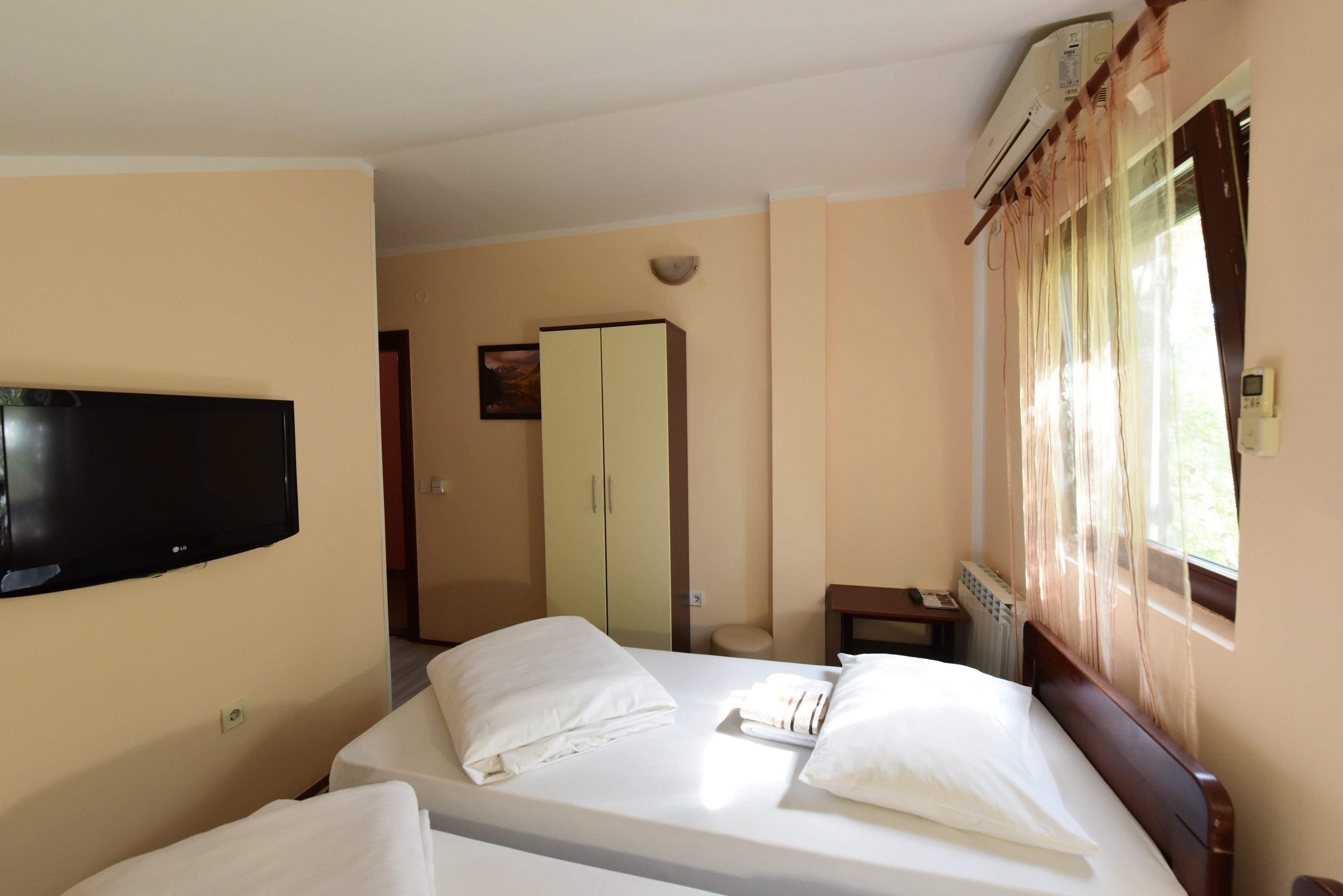 Ein Hotelzimmer mit Bett, Wandfernseher, Kleiderschrank und einem fenster mit Vorhängen.