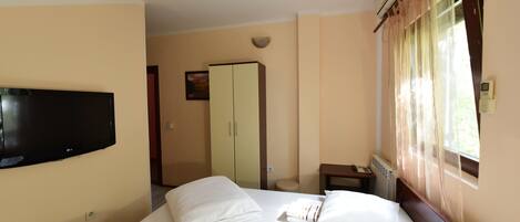 Habitación de hotel con cama, televisión montada en la pared, armario y ventana con cortinas.