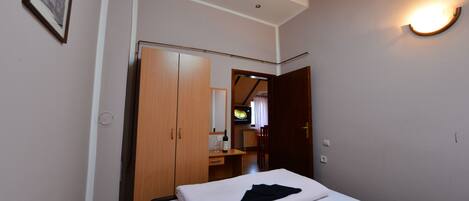 Quarto de hotel com cama, guarda-roupa, escrivaninha com cadeira, televisão e luminária na parede.