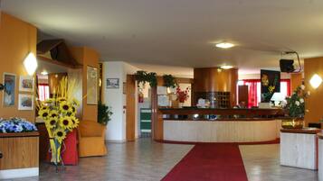 Un'accogliente hall d'hotel con reception, tappeto rosso e composizione floreale.