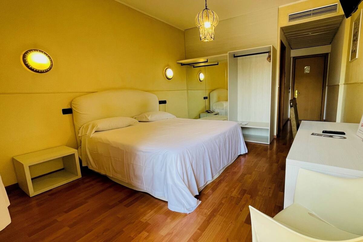 Ein Hotelzimmer mit Bett, Nachttischen, einem Schreibtisch und einem Spiegel.