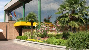 Un edificio con fachada de vidrio, elementos estructurales verdes y un jardín ajardinado con diversas plantas y flores.