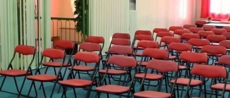 Un salón de conferencias con filas de sillas rojas, una mesa y una alfombra verde.