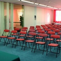 Une salle de conférence avec des rangées de chaises rouges, une table et une moquette verte.