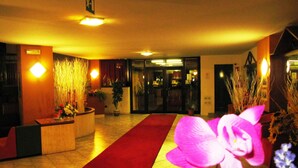 Un vestíbulo de hotel con alfombra roja, plantas en macetas y un mostrador de recepción.