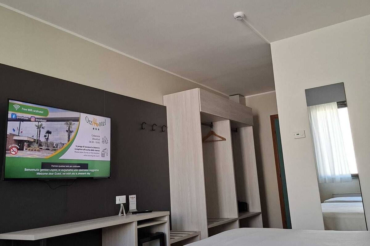 Ein Hotelzimmer mit einem Bett, einem an der Wand befestigten Fernseher und einem Kleiderständer.