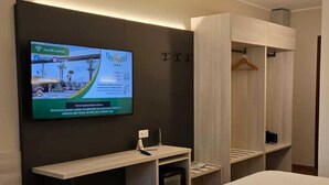 Habitación de hotel con dos camas, un televisor montado en la pared, un escritorio y un armario.