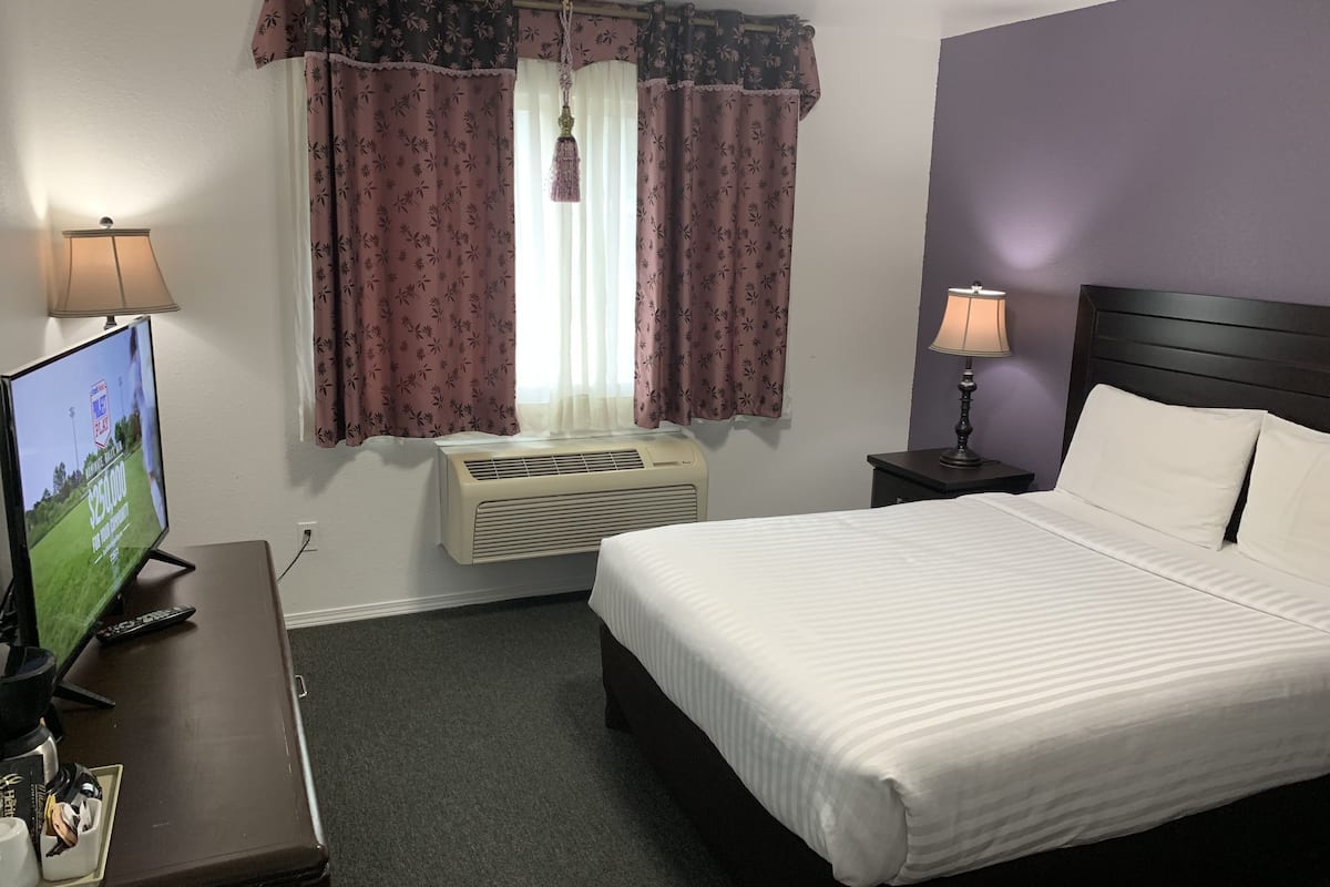 Ein Hotelzimmer mit einem Bett, einem Schreibtisch mit Fernseher, einer Lampe und einer Klimaanlage.
