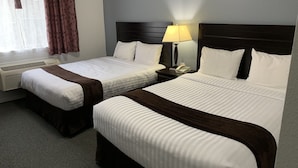 A hotel room with two beds, a bedside table with a lamp, a phone, and a window with curtains. - Lake Country Inn (Lake Country)