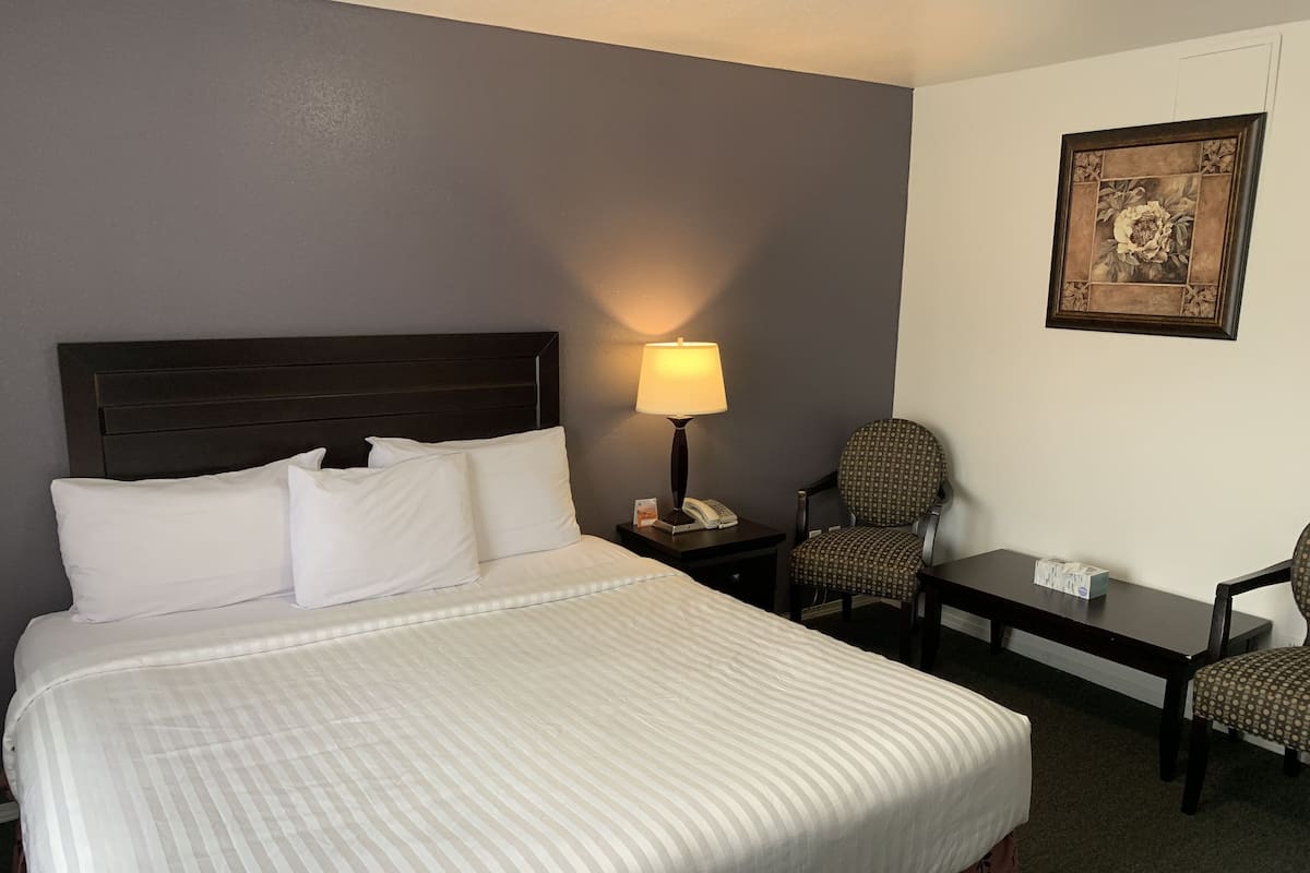 Ein Hotelzimmer mit einem großen Bett, einem Nachttisch mit Lampe, einem Sessel und einem kleinen Tisch.