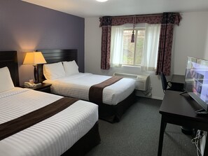 A hotel room with two beds, a desk, a TV, a phone, and a window with curtains.