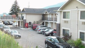A parking lot with several cars, a Coca-Cola vending machine, and a building with a balcony. - Lake Country Inn (Lake Country)