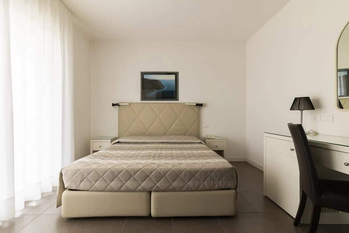A bedroom with a bed, bedside tables, a desk, and a chair.