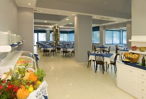 A spacious dining area with multiple tables and chairs, a buffet with various food items, and a decorative plant arrangement. - Hotel Miami (Jesolo)