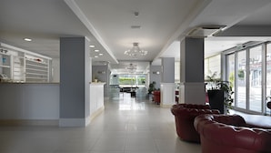 A spacious lobby with a reception desk, seating area, and large windows offering a view of the street. - Hotel Miami (Jesolo)