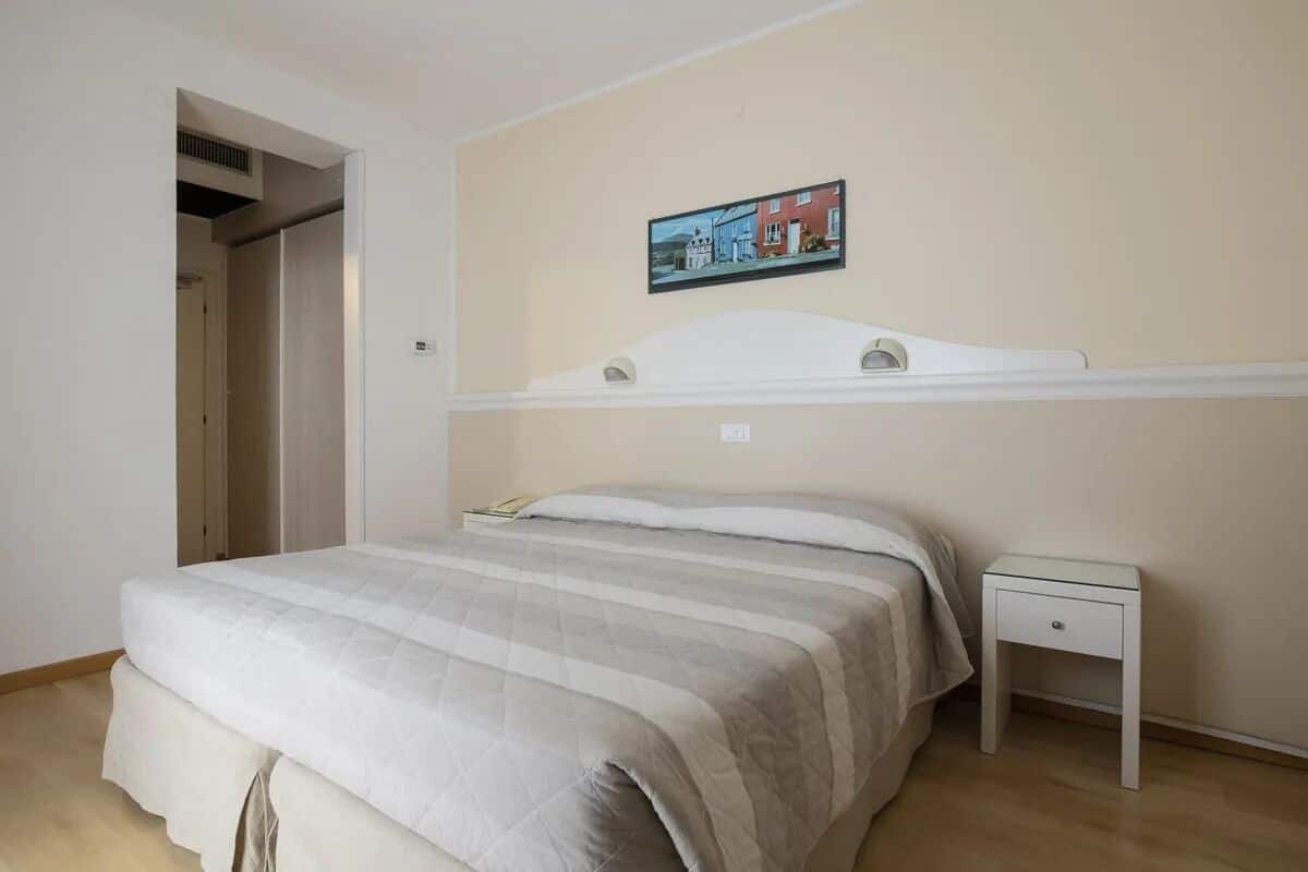 A bedroom with a bed, a nightstand, a painting on the wall, and a door leading to another room.