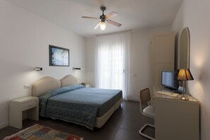 A bedroom with a bed, a desk, a chair, a TV, and a ceiling fan. - Hotel Miami (Jesolo)