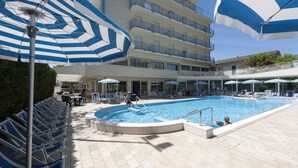 A pool area with blue and white striped umbrellas, lounge chairs, and a building with balconies. - Hotel Miami (Jesolo)