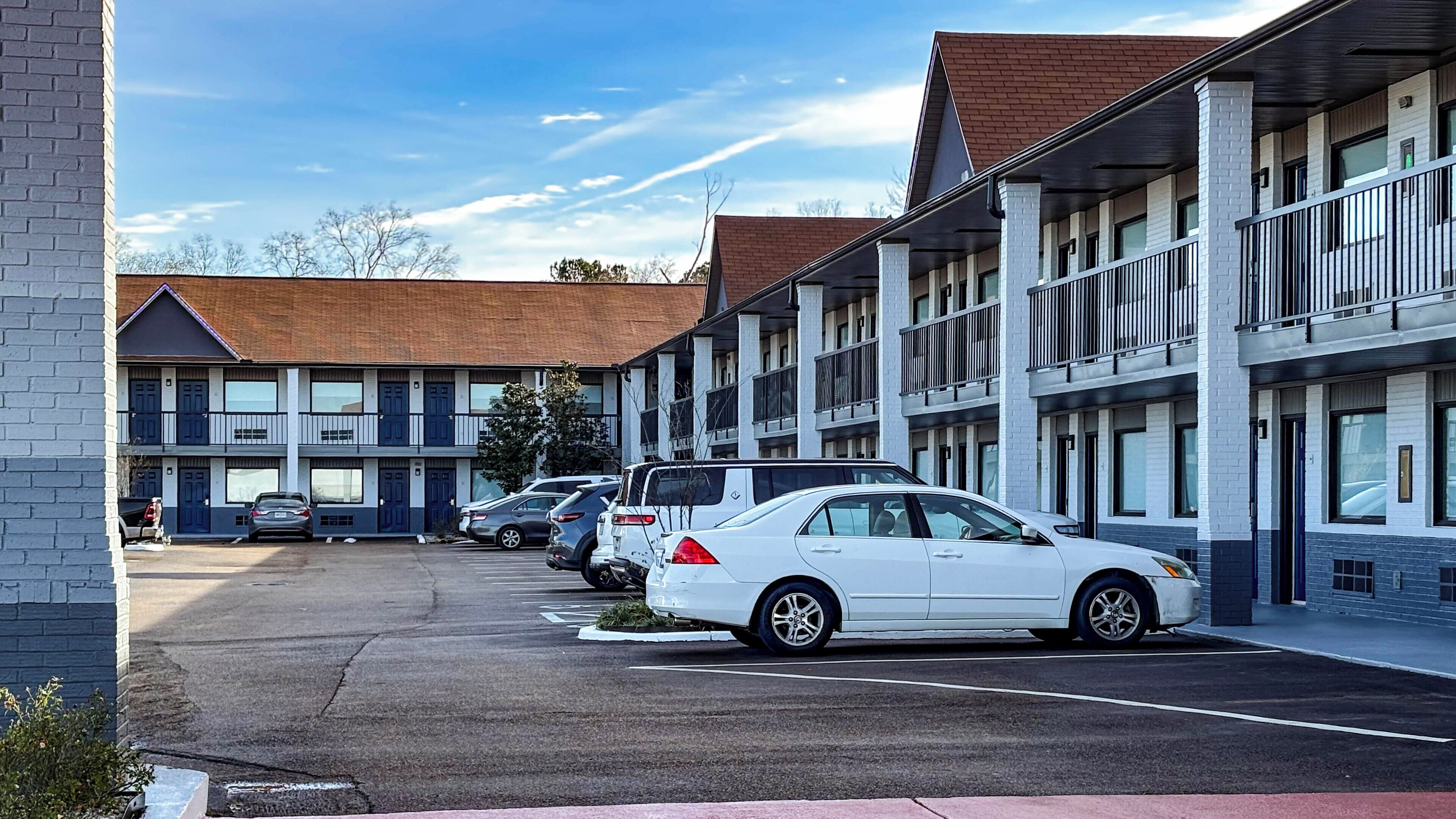 A motel with multiple-story buildings, a parking lot with several cars, and a clear sky.