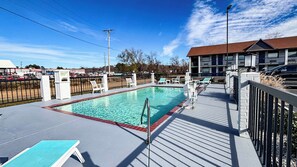 A rectangular swimming pool with a deck, surrounded by white lounge chairs and a metal fence.