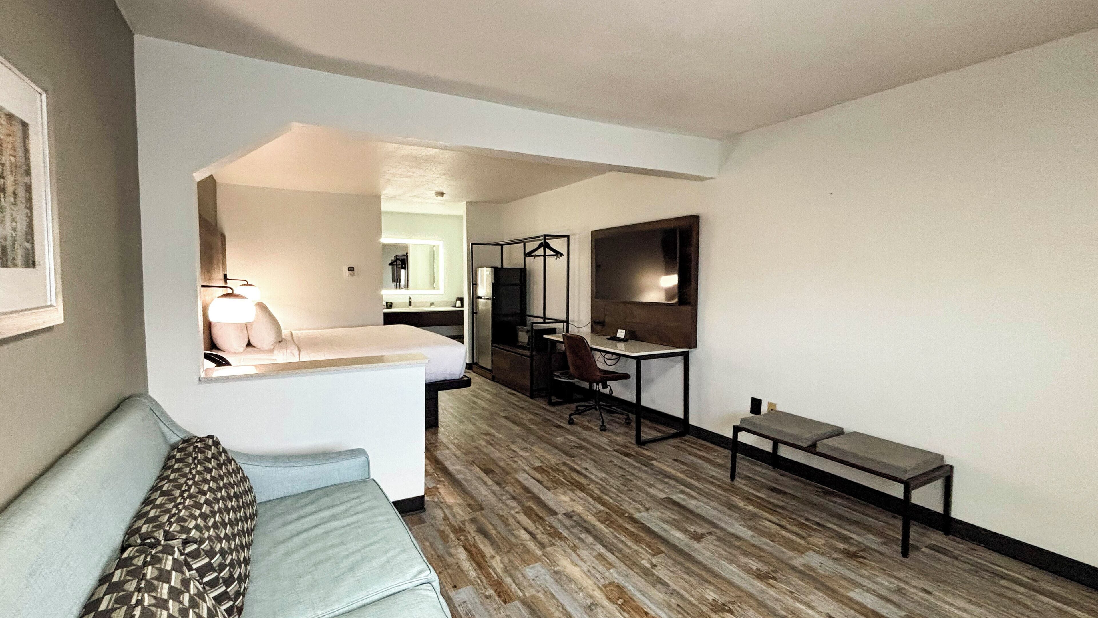 A modern hotel room with a sofa, a desk, and a small seating area.