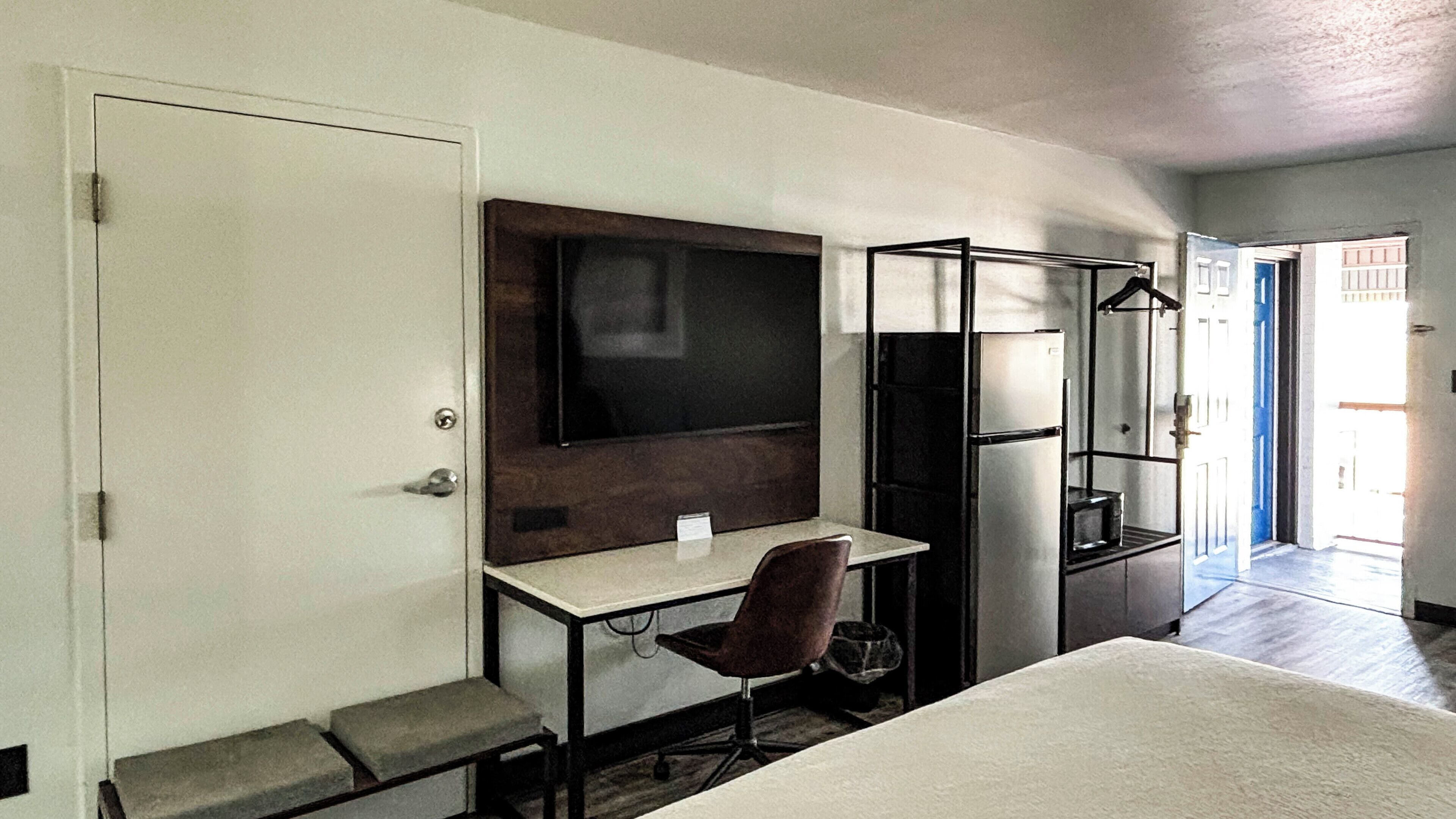 A compact hotel room with a single bed, a desk with a chair, a flat-screen TV, a small refrigerator, and a wardrobe.